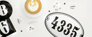 Home number signs: Close up of white house number sign on a table with a coffee and butterfly